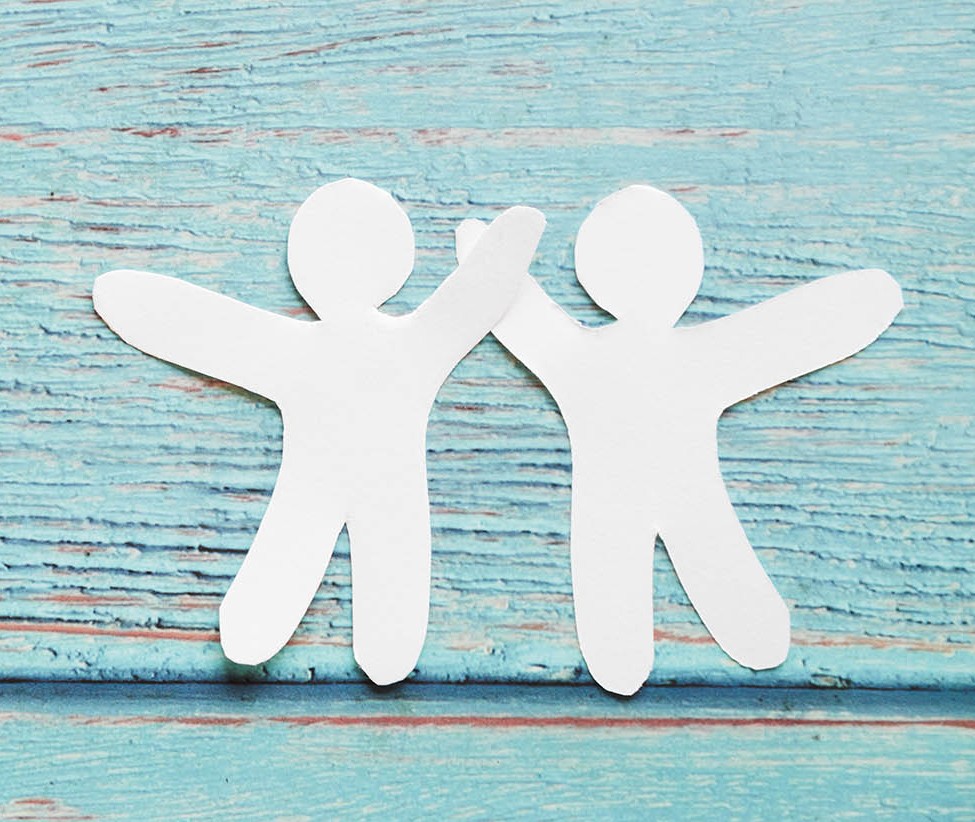 Zwei weiße Papierfiguren geben sich auf blauem Holz-Hintergrund die Hand.